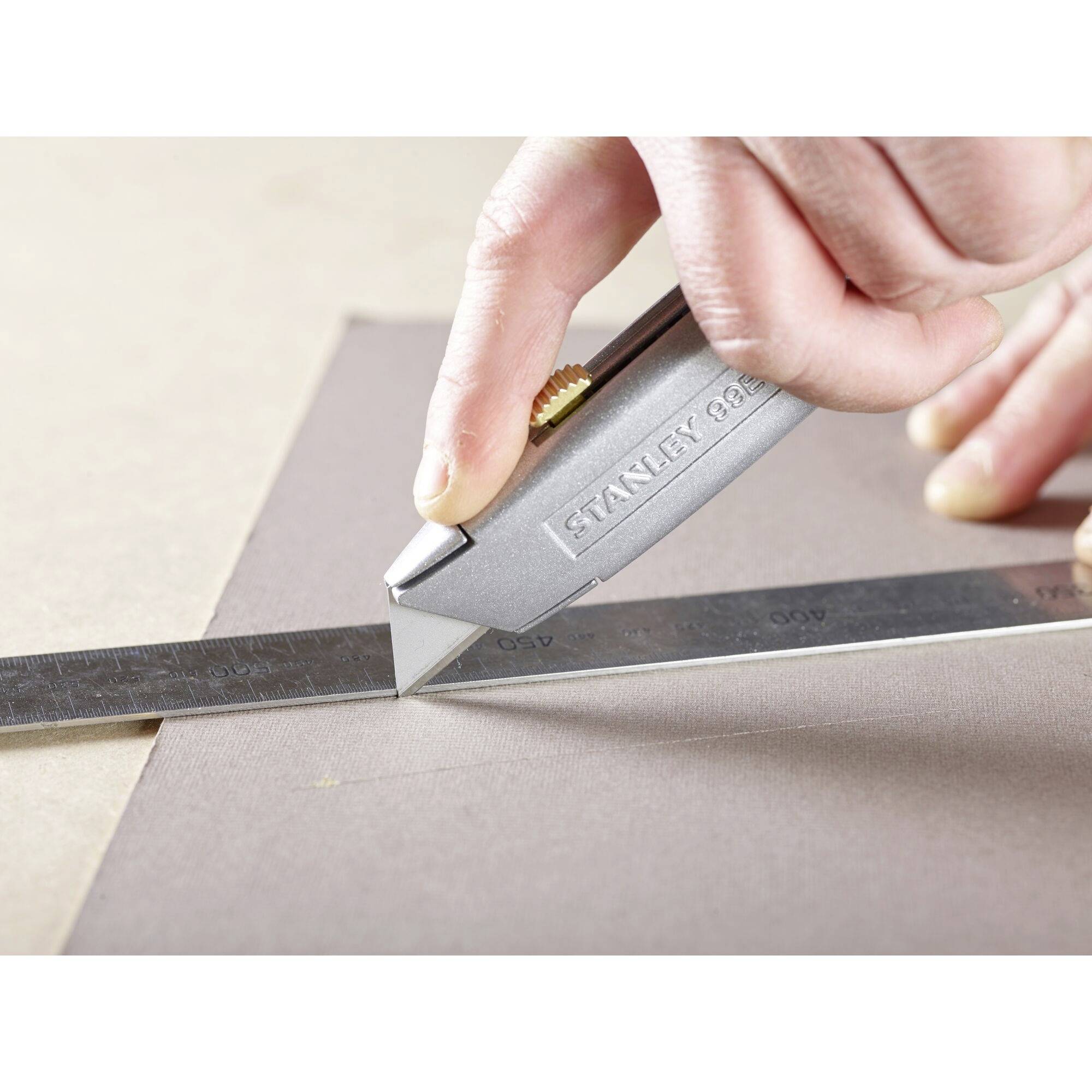 Une main tient un couteau à tapis qui est tiré le long d'une règle métallique sur une feuille de papier.