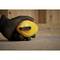 Une main gantée de noir tient un mètre ruban jaune, traçant une ligne bleue sur un plancher en bois.