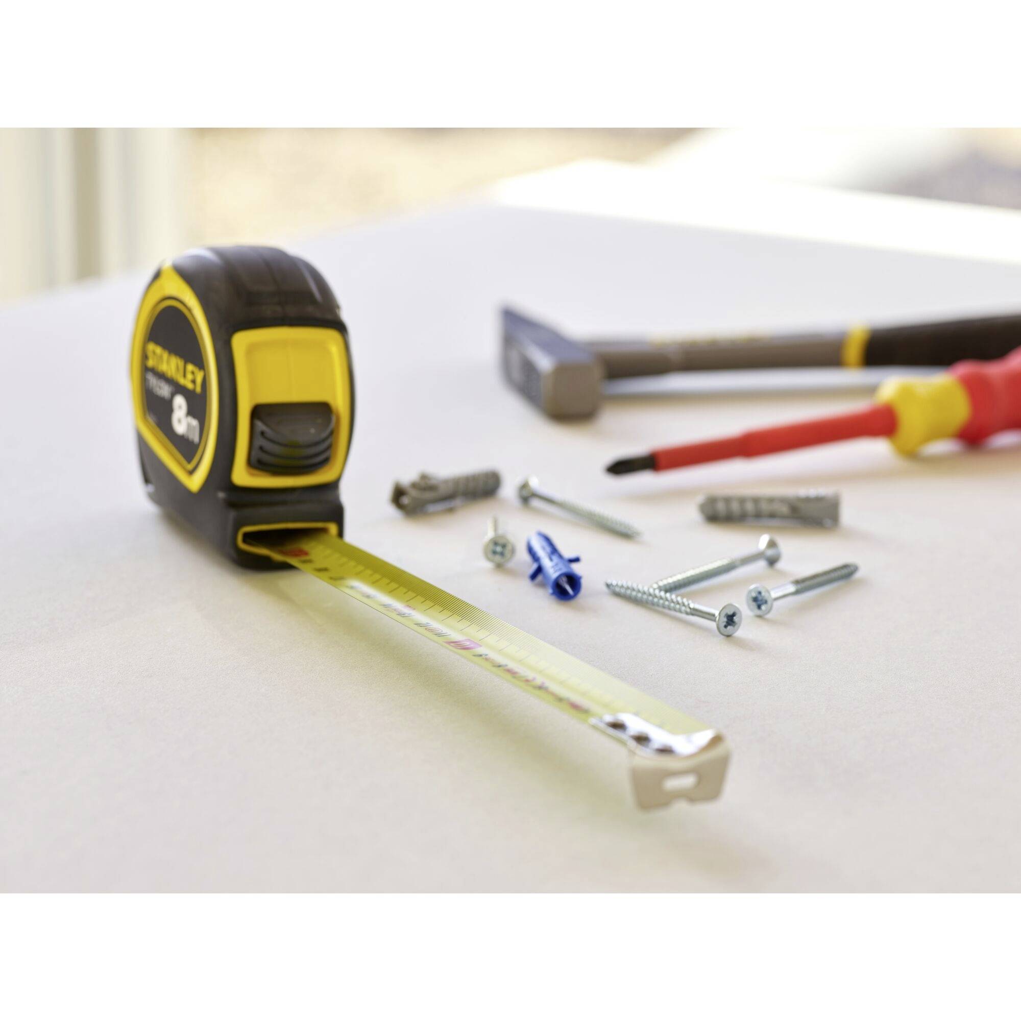 Un mètre ruban est posé sur une table à côté de vis, de chevilles et d'un tournevis, prêt pour un projet de bricolage.