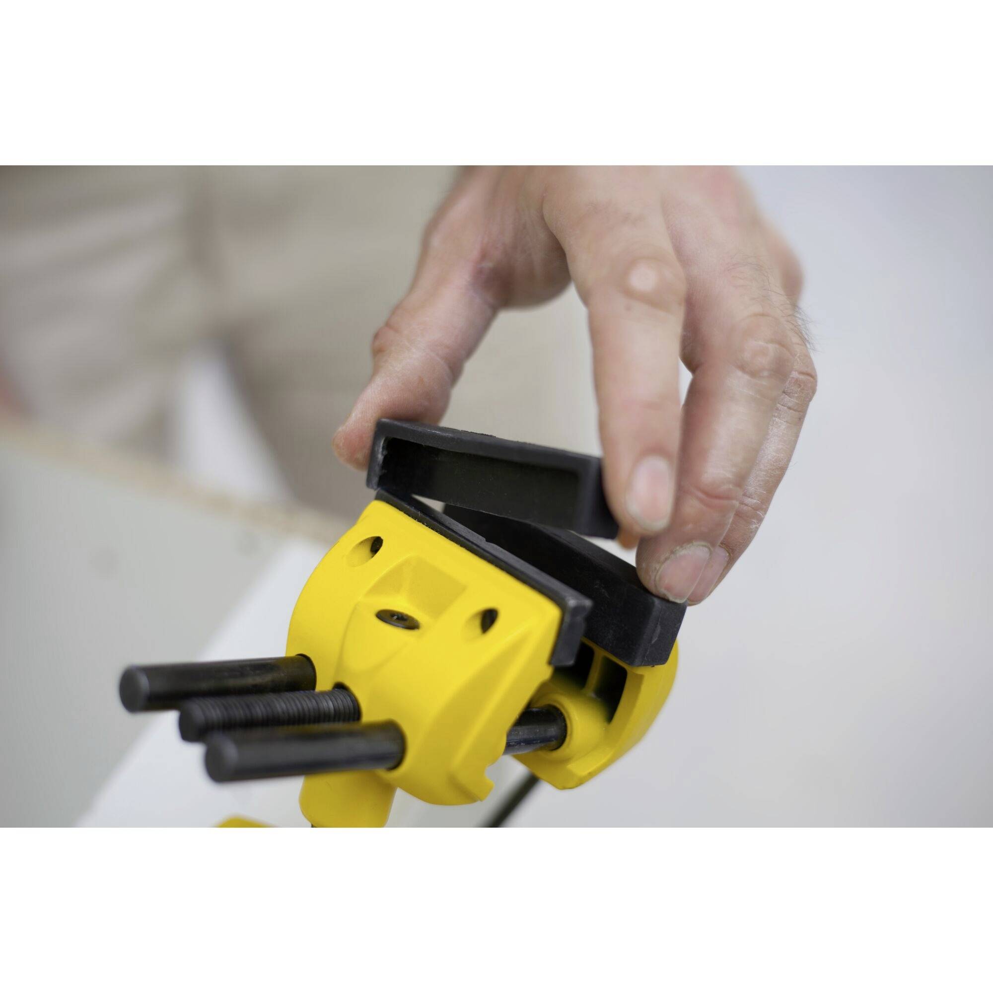 Une main ajuste un serre-joint jaune sur un établi. La scène montre la préparation des outils pour maintenir fermement des pièces de travail en toute sécurité.