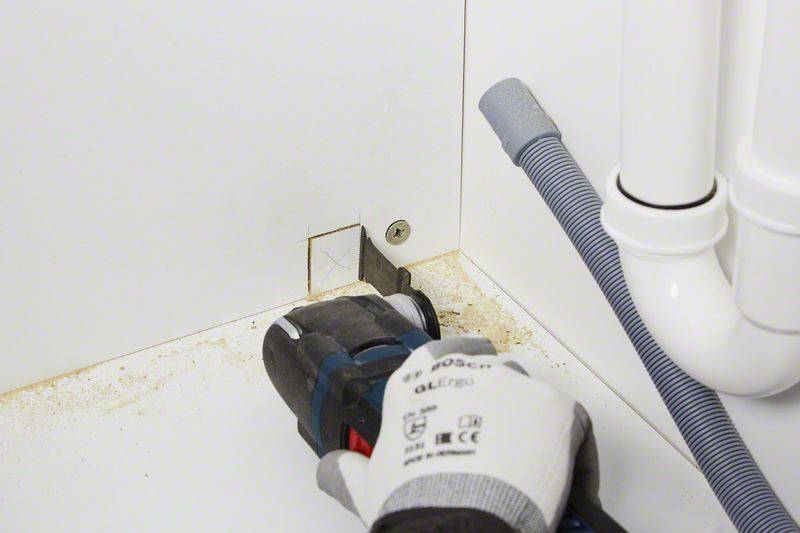 Un artisan découpe un trou carré dans un mur blanc à l'aide d'un outil électrique pour installer des tuyaux.