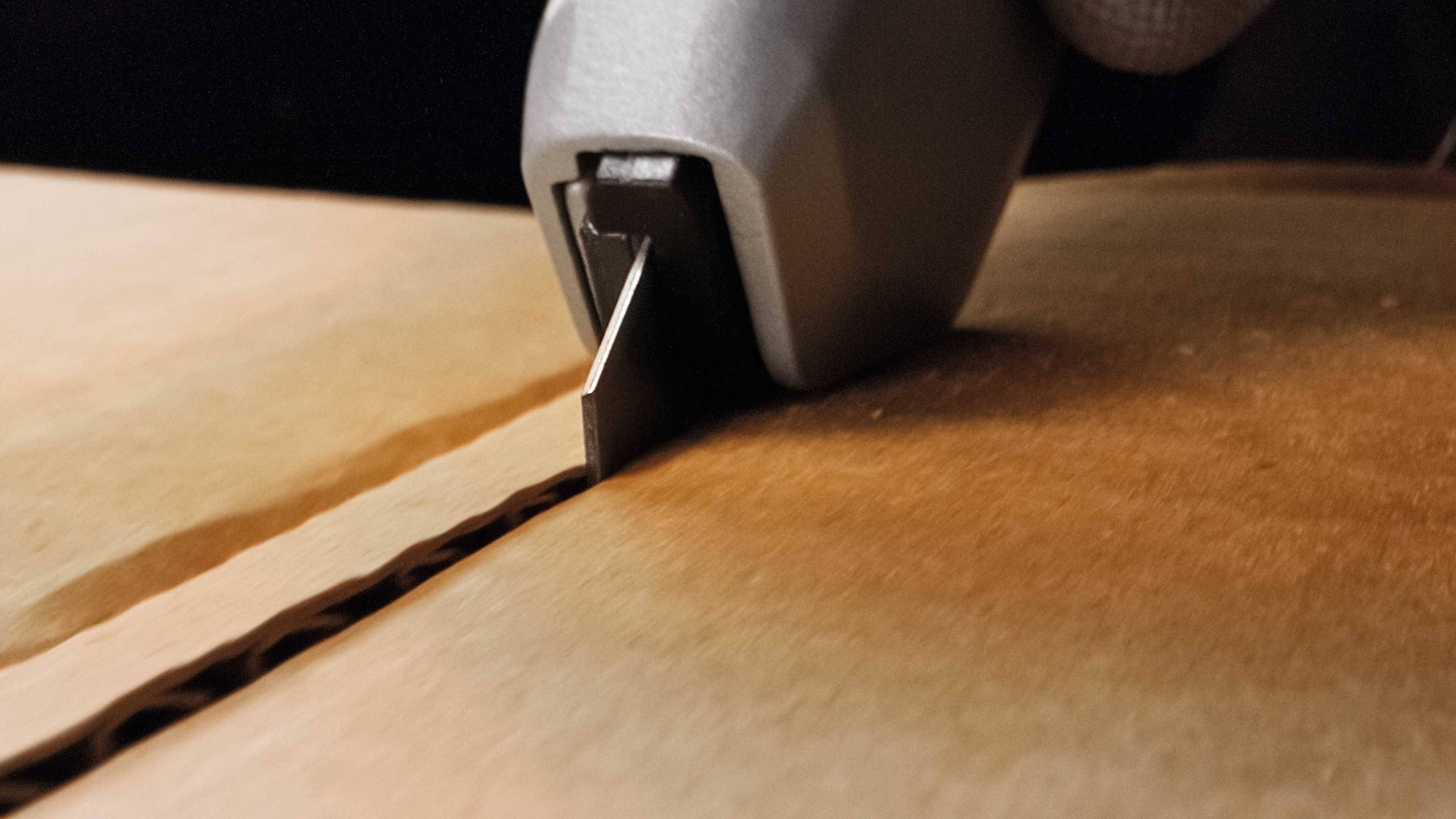 Gros plan sur une main utilisant un cutter pour ouvrir un carton. La mise au point est sur la lame et la ligne de coupe dans le carton.