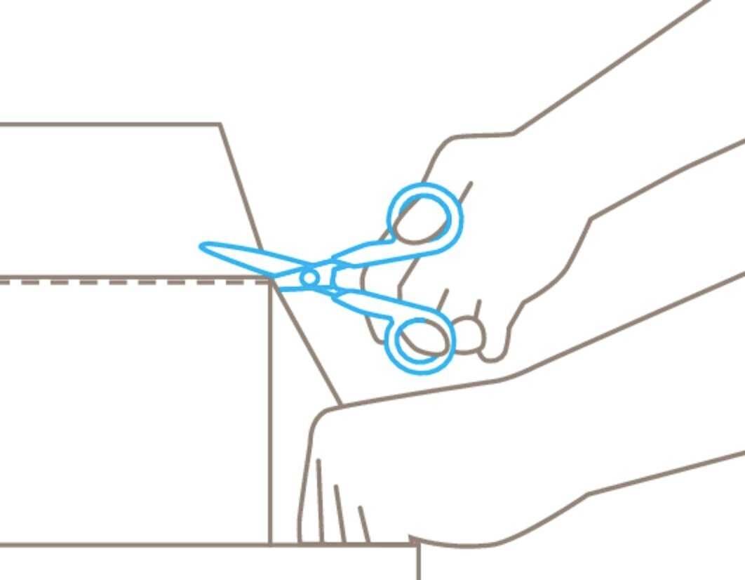 Une main tient des ciseaux pour couper une ligne pointillée sur un carton.