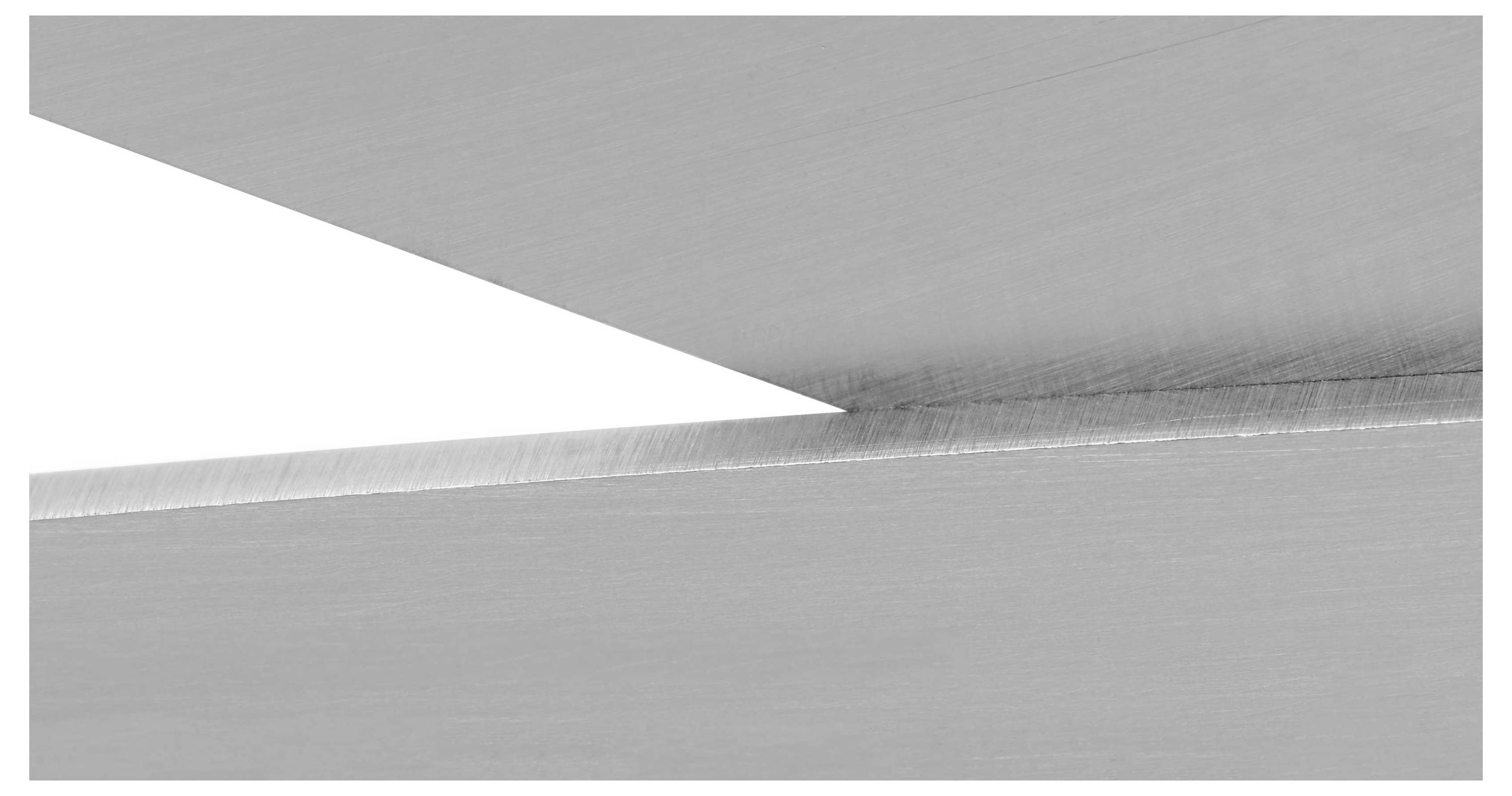 Gros plan de deux bords métalliques qui se croisent dans un environnement industriel. Les surfaces sont lisses et reflètent la lumière.