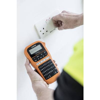 Une personne installe ou vérifie une prise électrique tout en tenant un appareil d'étiquetage orange dans l'autre main.