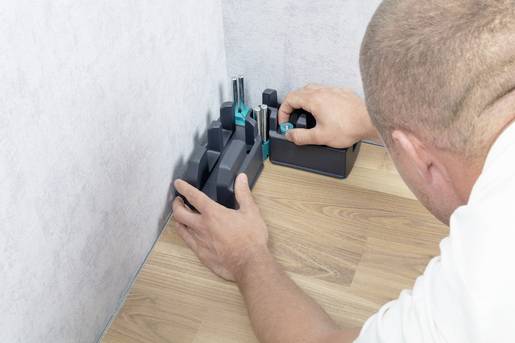 'Un homme utilise un outil de mesure pour ajuster précisément l'angle entre un mur et le sol, probablement lors de travaux de rénovation.'