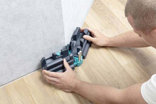 Une personne utilise un outil pour la pose de sol stratifié afin d'ajuster précisément les découpes le long du mur.