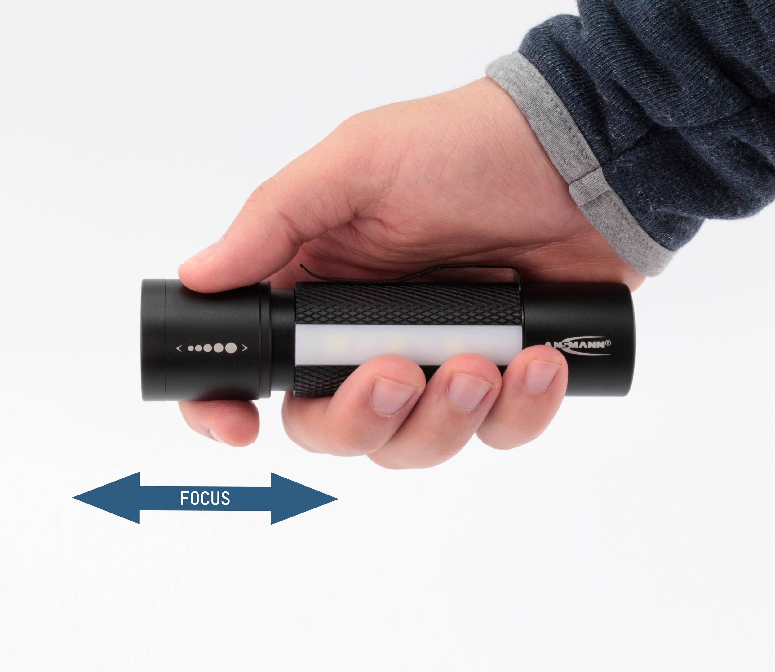 Une main tient une lampe de poche avec une flèche de direction de focus en dessous. La lampe dispose d'un focus rotatif permettant des réglages d'éclairage variables.