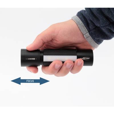 Une main tient une lampe de poche avec une flèche de direction de focus en dessous. La lampe dispose d'un focus rotatif permettant des réglages d'éclairage variables.