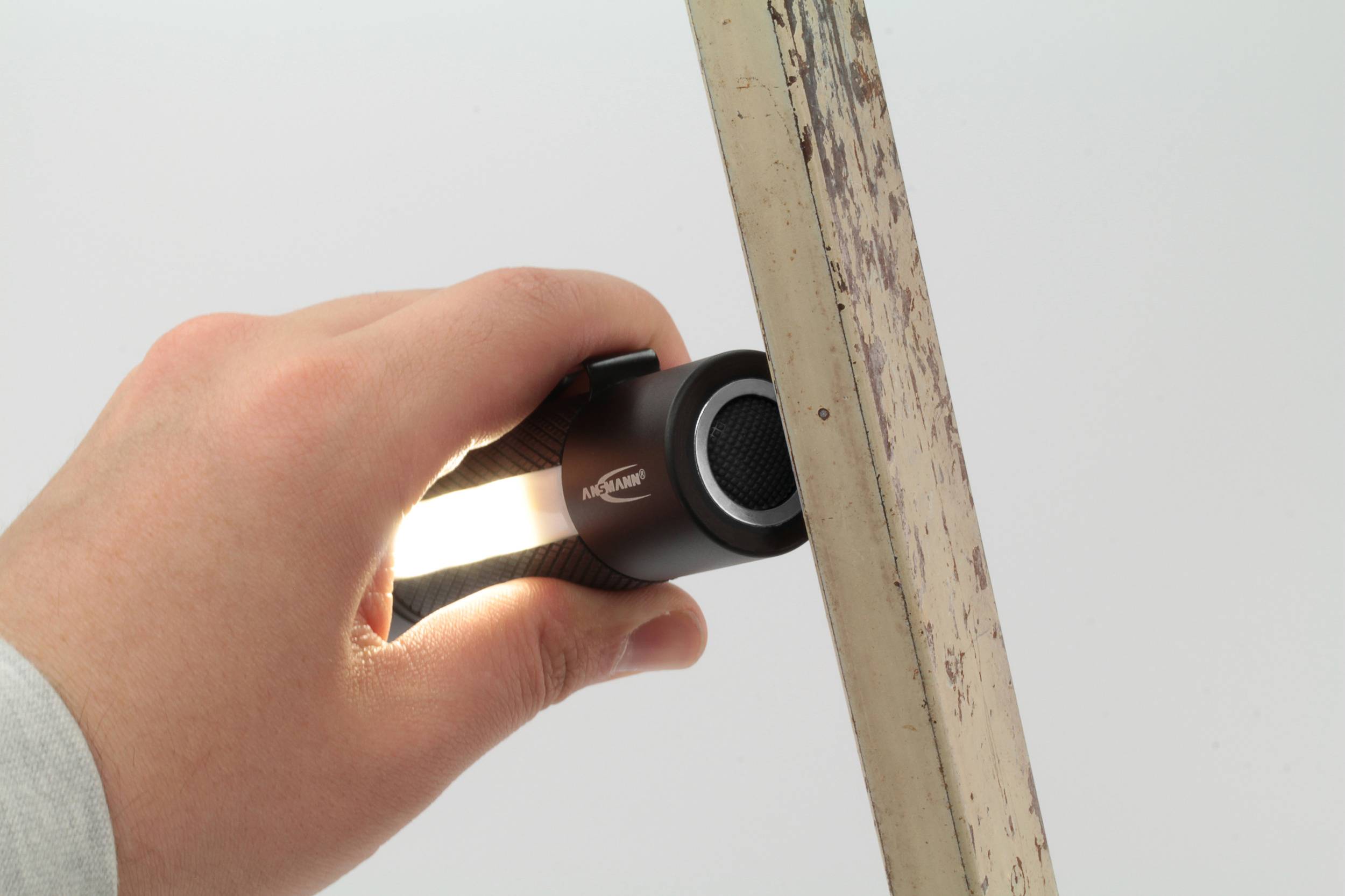 Une main tient une petite lampe de poche projetant sa lumière le long d'un objet métallique vertical.