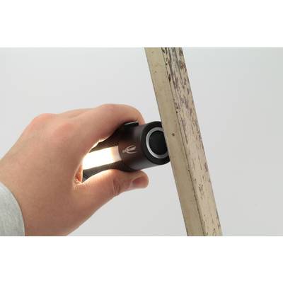Une main tient une petite lampe de poche projetant sa lumière le long d'un objet métallique vertical.