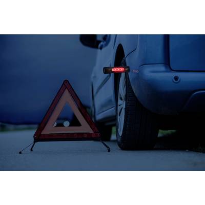 Un triangle de signalisation clignotant est placé près d'une voiture garée en bordure de route au crépuscule, afin de prévenir un danger potentiel.