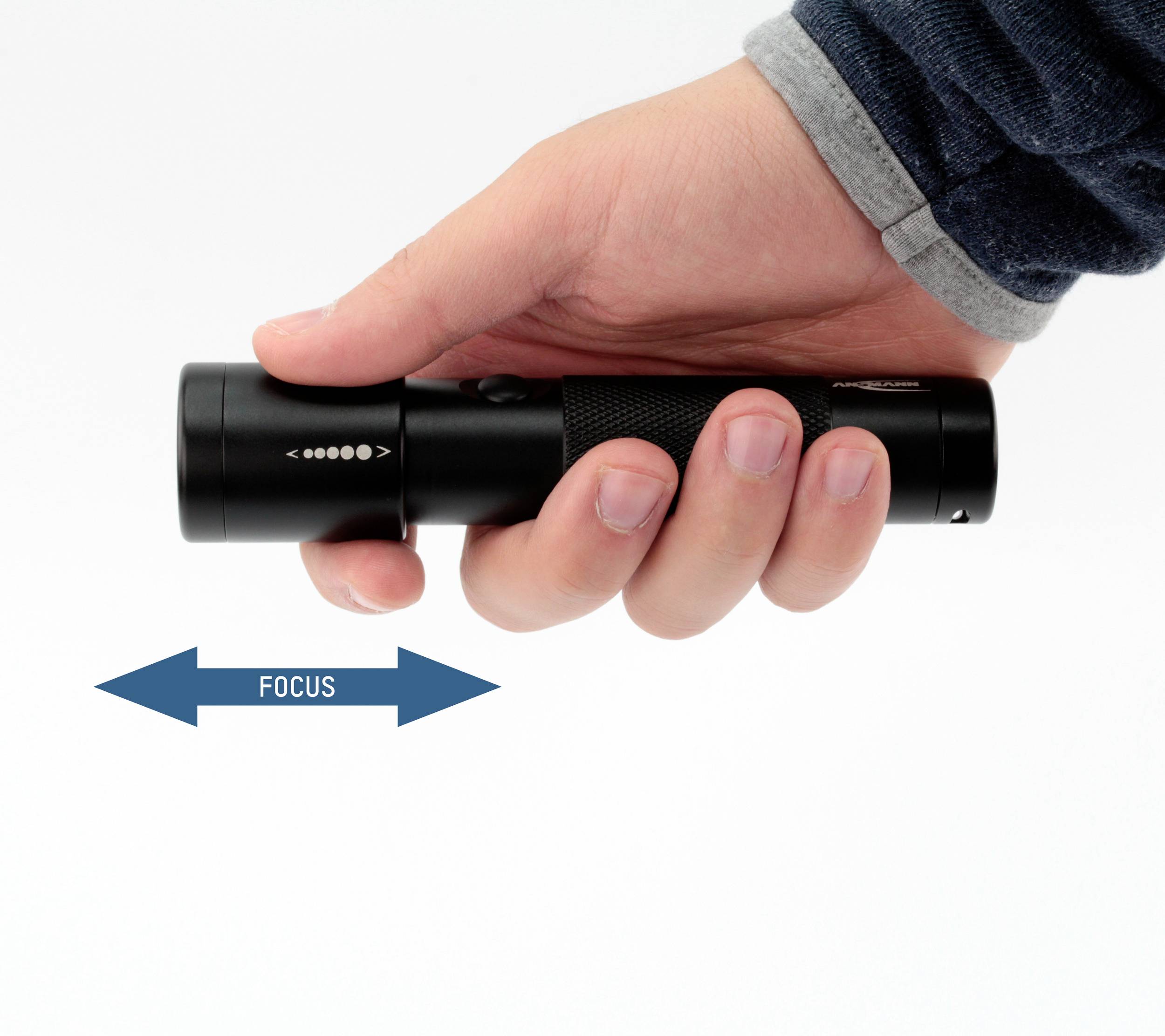 Une main tient une lampe de poche noire ; une flèche en dessous indique le réglage de la mise au point, avec une indication 'FOCUS' montrant la direction.