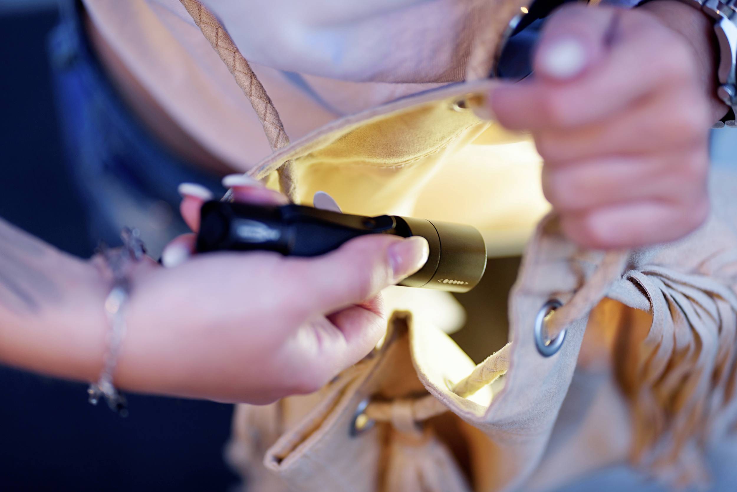 Une personne ouvre un sac dans lequel on braque une petite lampe de poche. La scène illustre une recherche concentrée d'un objet.