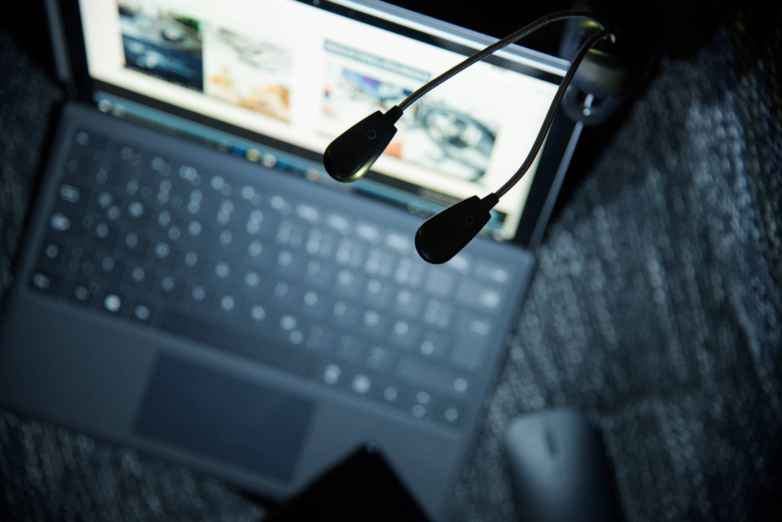Un ordinateur portable posé sur une table, son écran ouvert. Devant l'écran, deux lampes USB noires sont visibles.