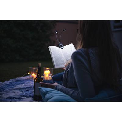 Une personne lit un livre à la lumière des bougies, dehors. À côté d'elle se trouvent une bouteille de vin et des verres. L'atmosphère est détendue.