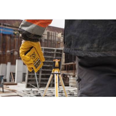 Une personne tient une télécommande jaune. En arrière-plan, un appareil de mesure est installé sur un trépied de chantier.