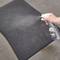 Une main vaporise un nettoyant intérieur de voiture sur un tapis noir à partir d'une bouteille afin d'éliminer les salissures.