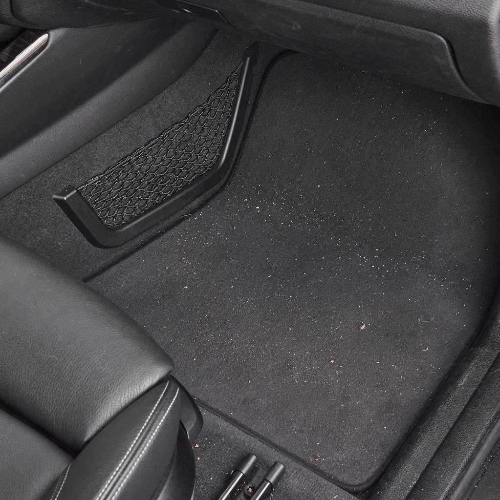 Habitacle de voiture avec un tapis de sol noir, quelques miettes et saletés sont visibles.