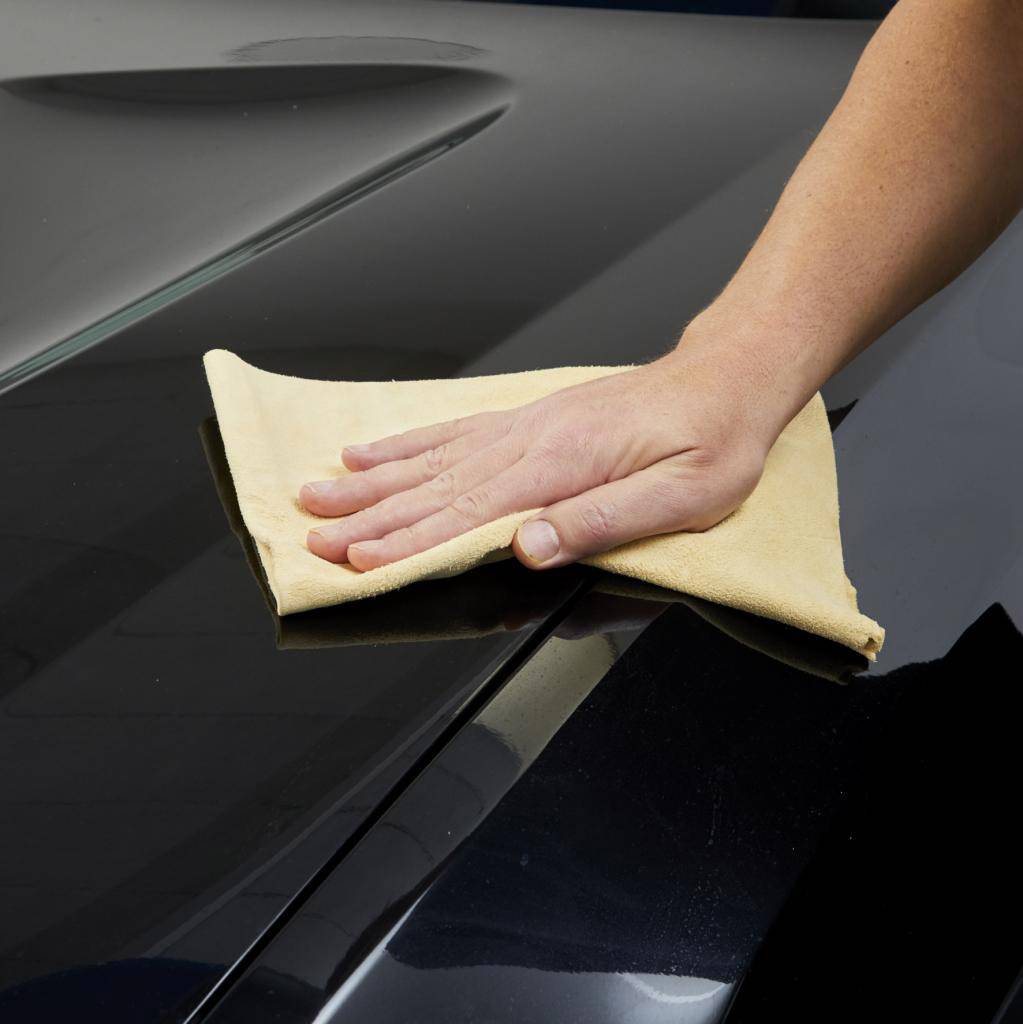 Une main essuie une surface brillante de vernis noir d'une voiture avec un chiffon jaune.