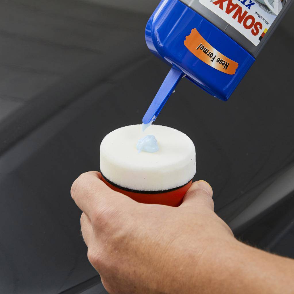 Une personne applique du vernis bleu sur un tampon applicateur rouge et blanc, le vernis provenant d'une bouteille étiquetée 'Nouvelle Formule'.