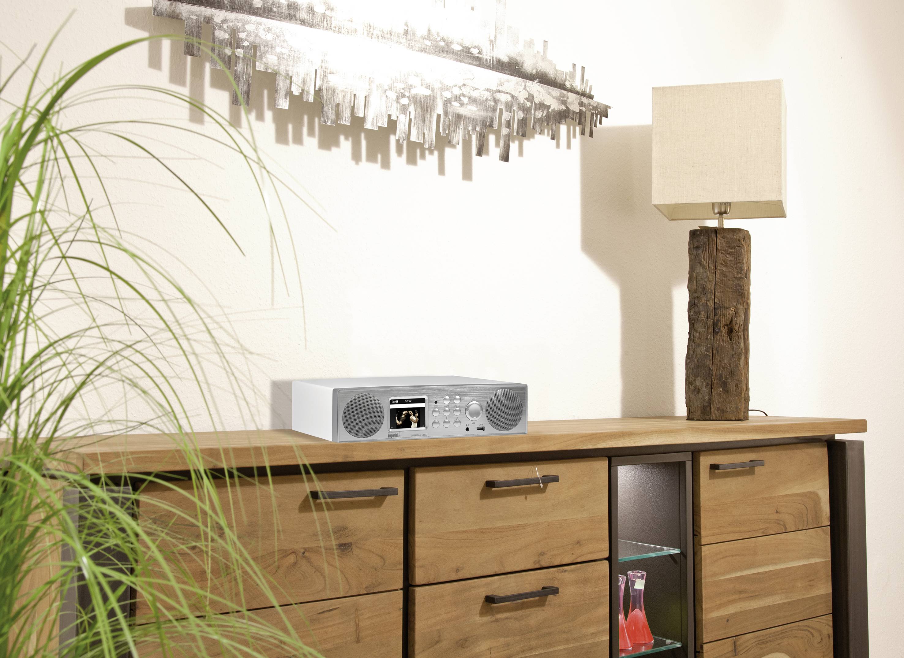 Radio sur une commode en bois dans une pièce au design moderne avec une plante d'intérieur, une lampe et une œuvre d'art abstraite au mur.