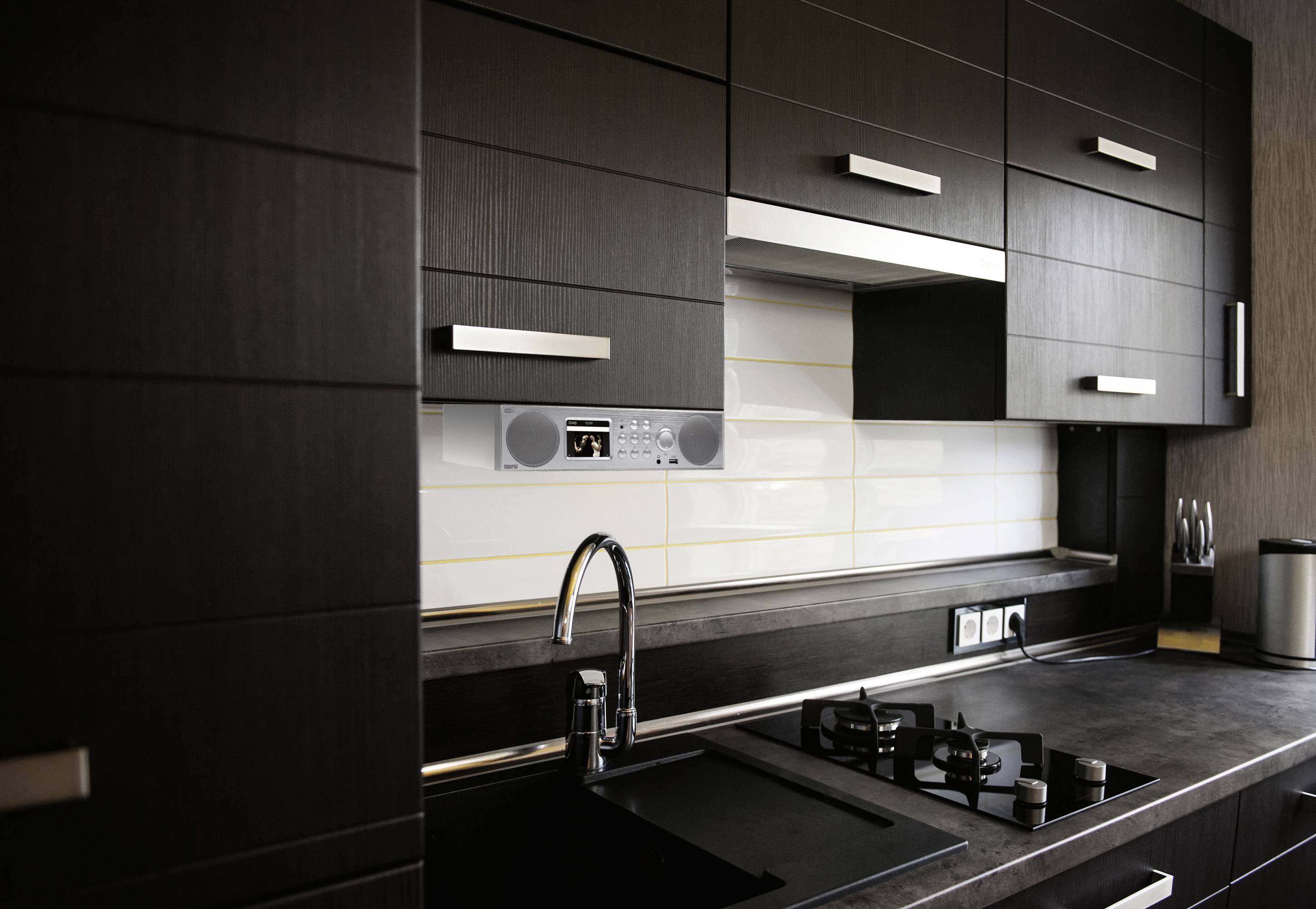 Cuisine moderne avec des armoires foncées, une cuisinière et un évier. Des carreaux clairs forment l'arrière-plan. Les prises électriques sont visibles.