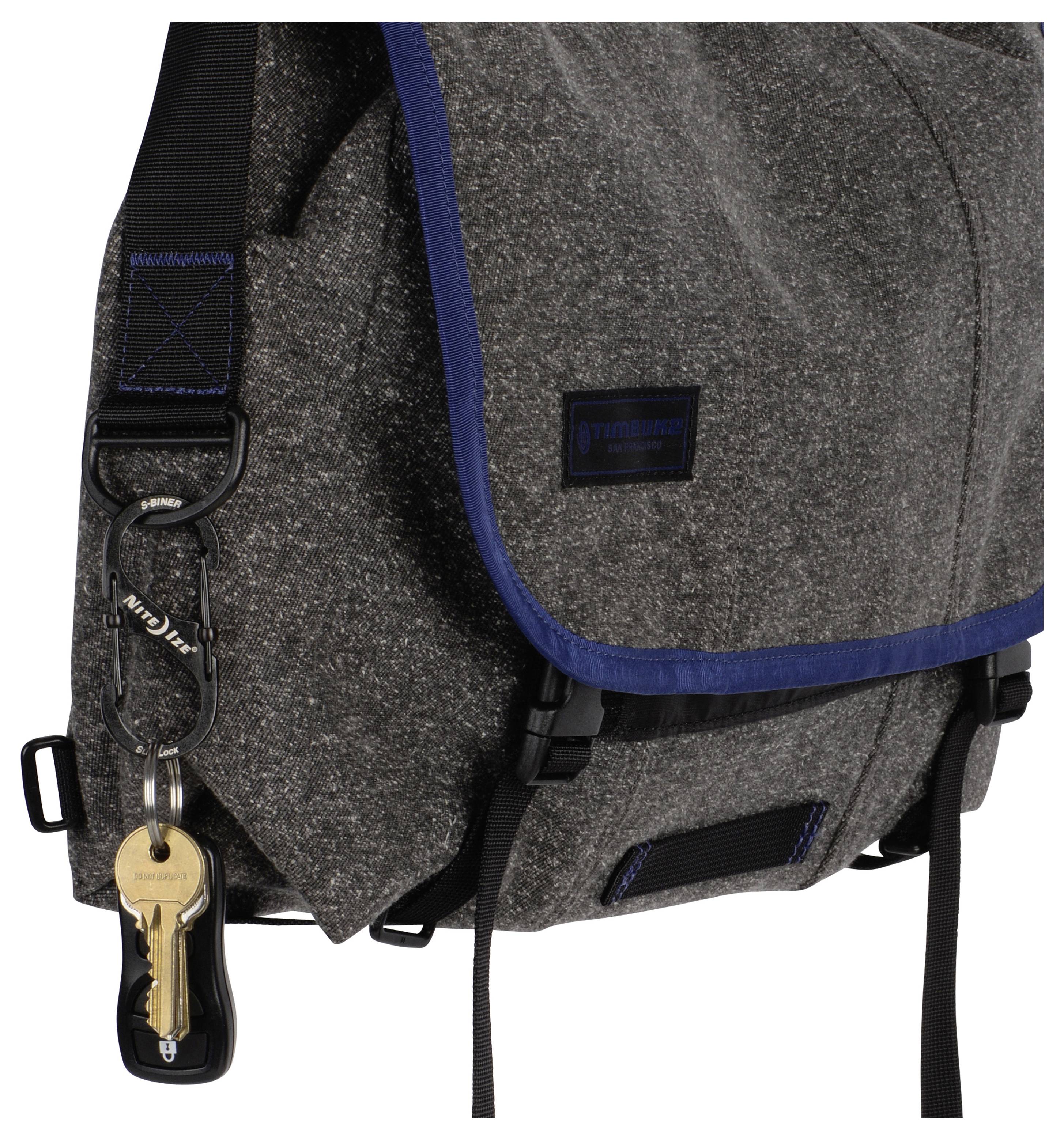 Un sac à bandoulière en tissu gris avec bordure bleue, muni d'un anneau porte-clés fixé à la sangle et portant des clés ainsi qu'un porte-clés.