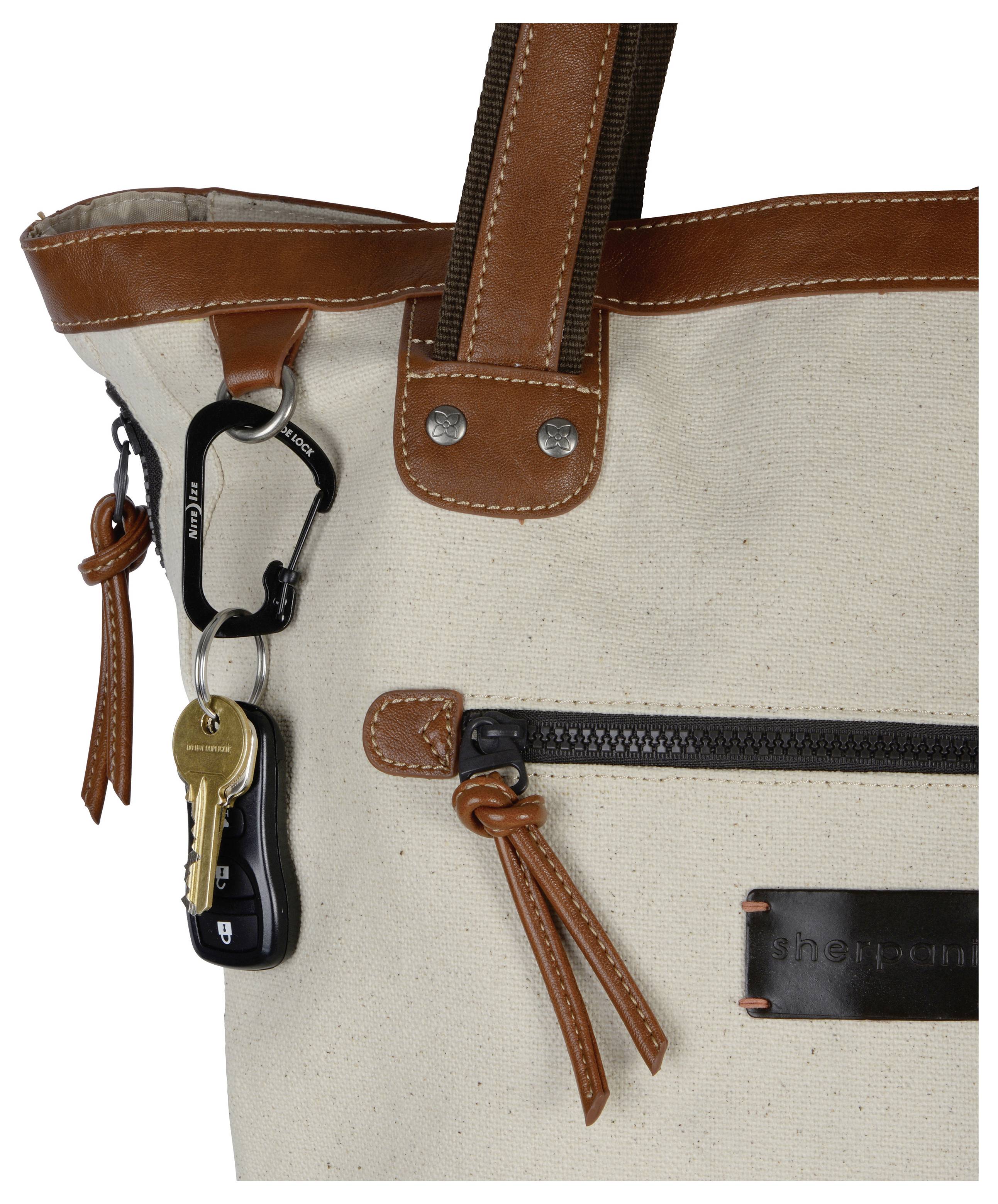 Un sac cabas beige avec bordure en cuir marron, doté d'une poche zippée à l'avant et d'un porte-clés attaché à la poignée retenant des clés accrochées.