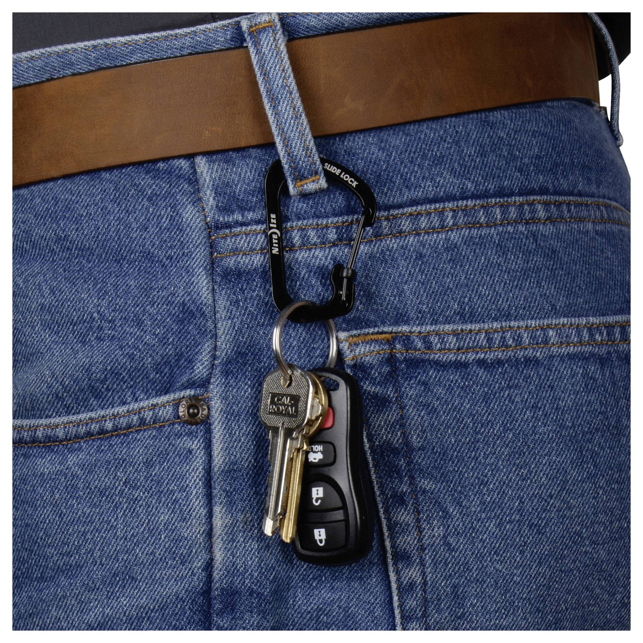 Un trousseau de clés et une télécommande de voiture sont attachés à un mousqueton accroché à une ceinture marron, portée avec un jean bleu.