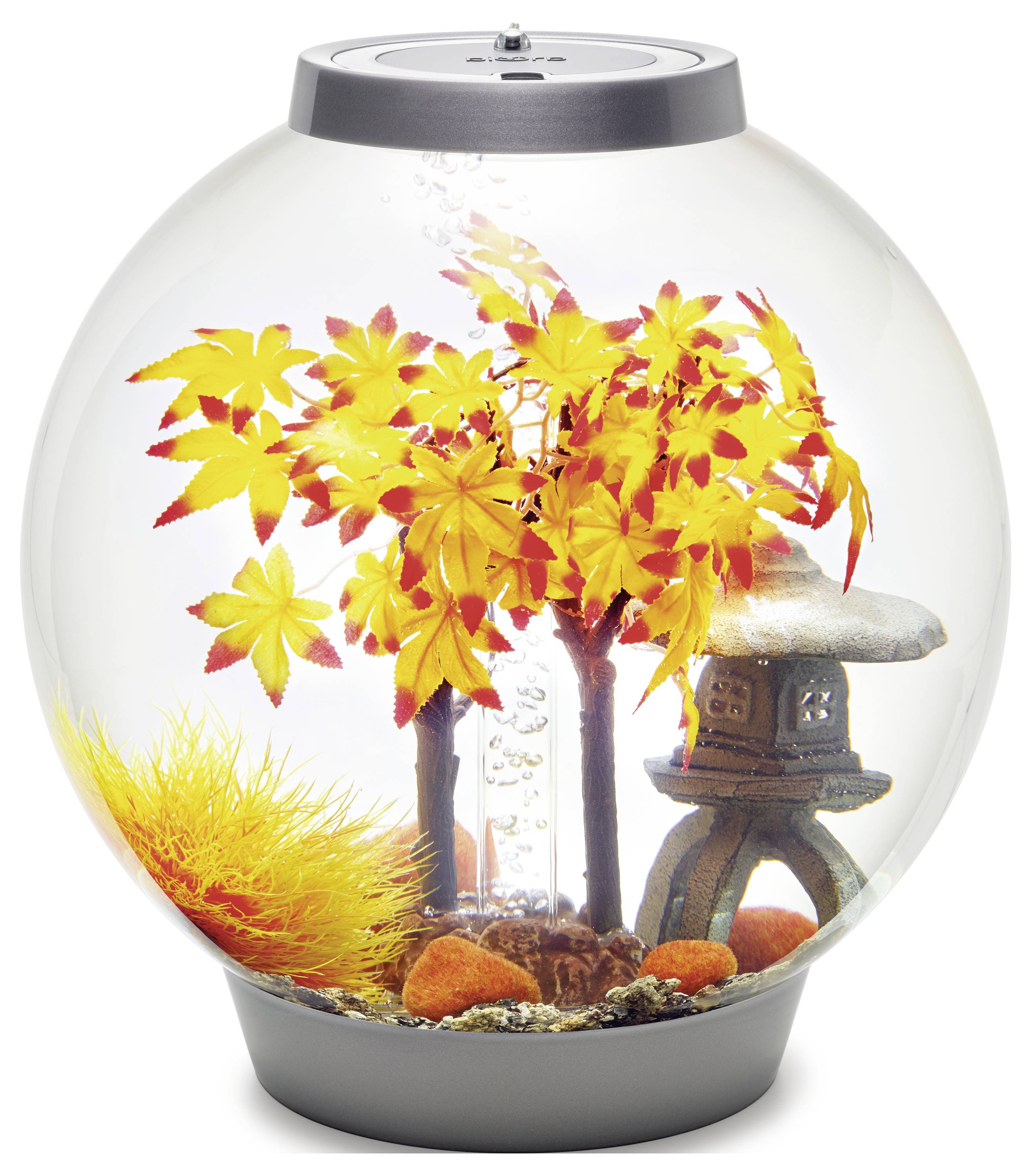 Un aquarium sphérique avec des feuilles d'automne décoratives, de petites statues et des pierres orangées, créant un affichage coloré et saisonnier.