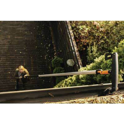 Une personne se tient en bas et regarde un toit. Un outil de nettoyage est utilisé pour retirer les feuilles de la gouttière.