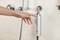 Une main appuie sur un bouton d'un distributeur de douche élégant et argenté, fixé sur la paroi d'une salle de bain, à côté d'accessoires de douche brillants en métal.
