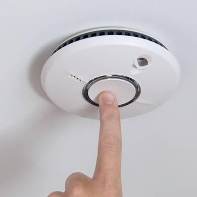 Une main appuyant sur le bouton de test d'un détecteur de fumée monté au plafond.