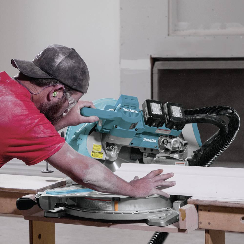 Un homme scie une planche en bois avec une scie circulaire dans un atelier. Il porte des protections auditives et des vêtements de protection.