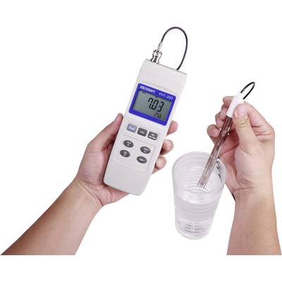 Une personne tient un appareil de mesure numérique avec une sonde dans un verre d'eau. L'écran affiche '0,03' et '25,6'.
