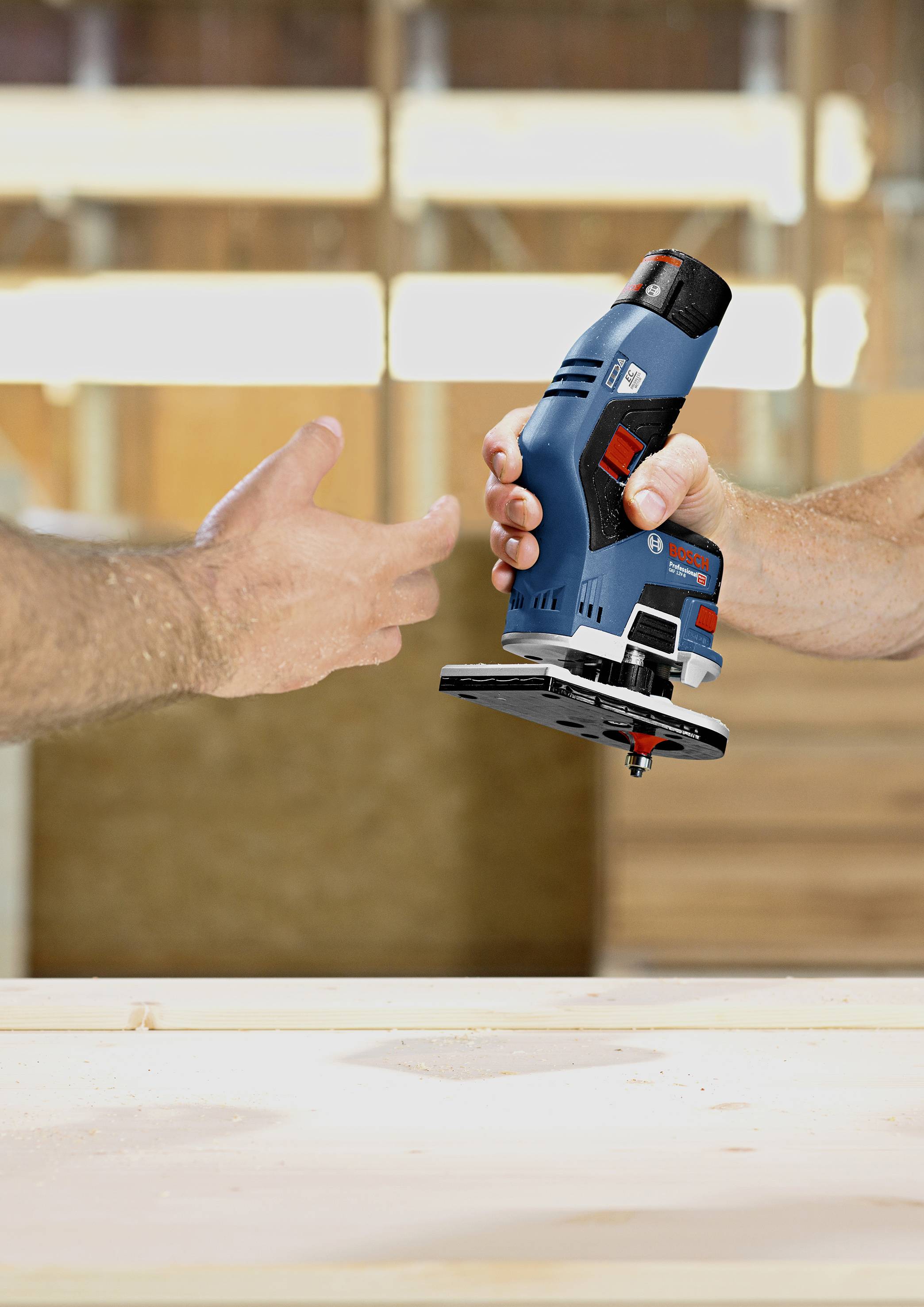 Une personne remet une fraiseuse électrique bleue à une autre personne dans un atelier de menuiserie.