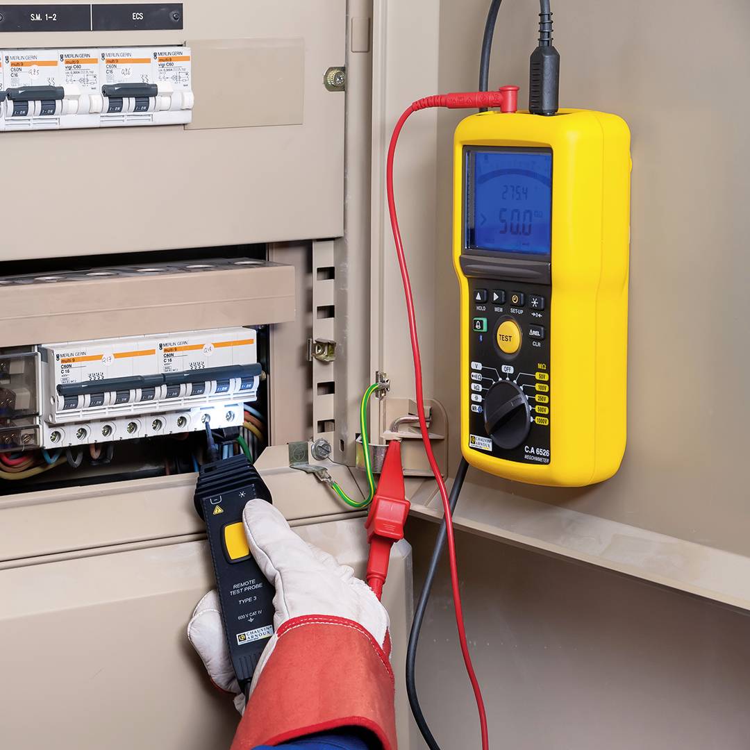 Un électricien mesure le flux de courant dans un coffret de distribution à l'aide d'un multimètre jaune.