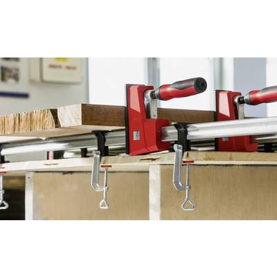 Un établi équipé de deux serre-joints rouge et noir, fixant une grande planche en bois. Les outils semblent solides et robustes.