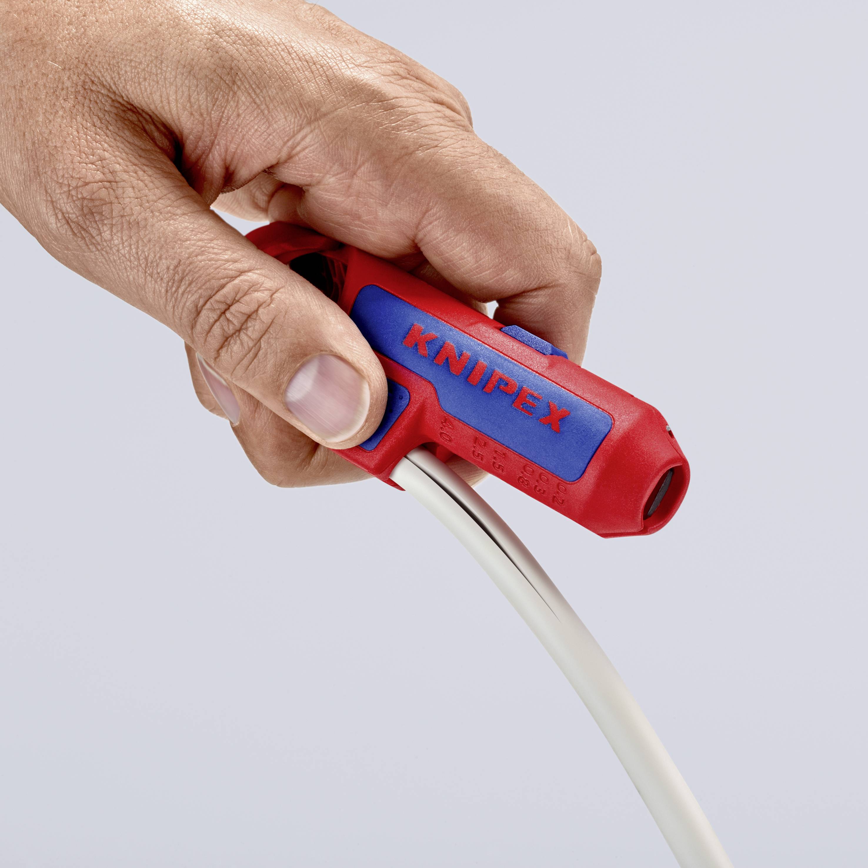 Une main tient un outil rouge de la marque Knipex, utilisé pour dénuder un câble blanc.