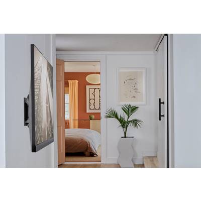 Un couloir moderne avec une fresque murale intégrée mène à une chambre aux murs oranges et aux meubles blancs. Un palmier se dresse devant.