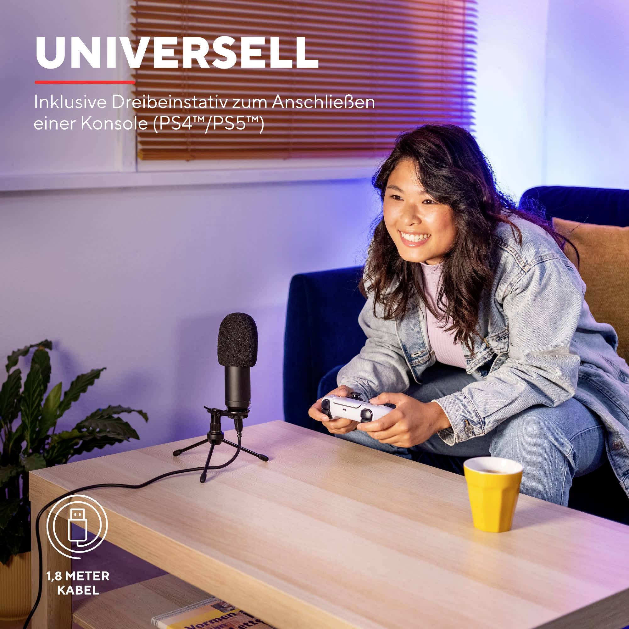 Une femme souriante est assise sur un canapé et tient une manette de jeu. Un microphone est posé sur une table à côté d'elle.