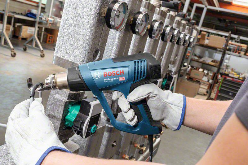 Une personne tient un pistolet thermique Bosch et traite une pièce technique dans un environnement industriel.