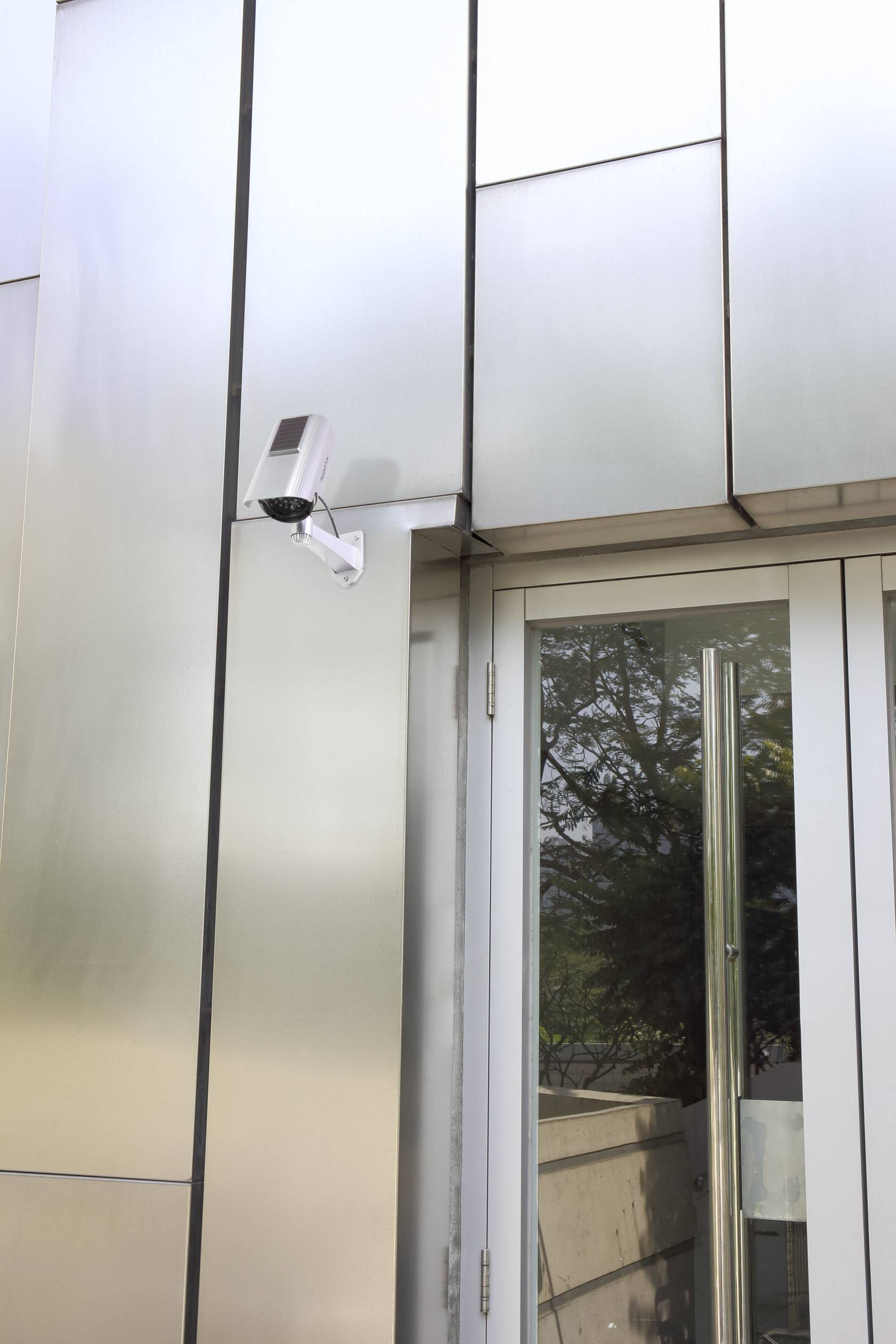 Caméra de sécurité fixée sur le mur extérieur d'un bâtiment moderne, installée au-dessus d'une porte vitrée.