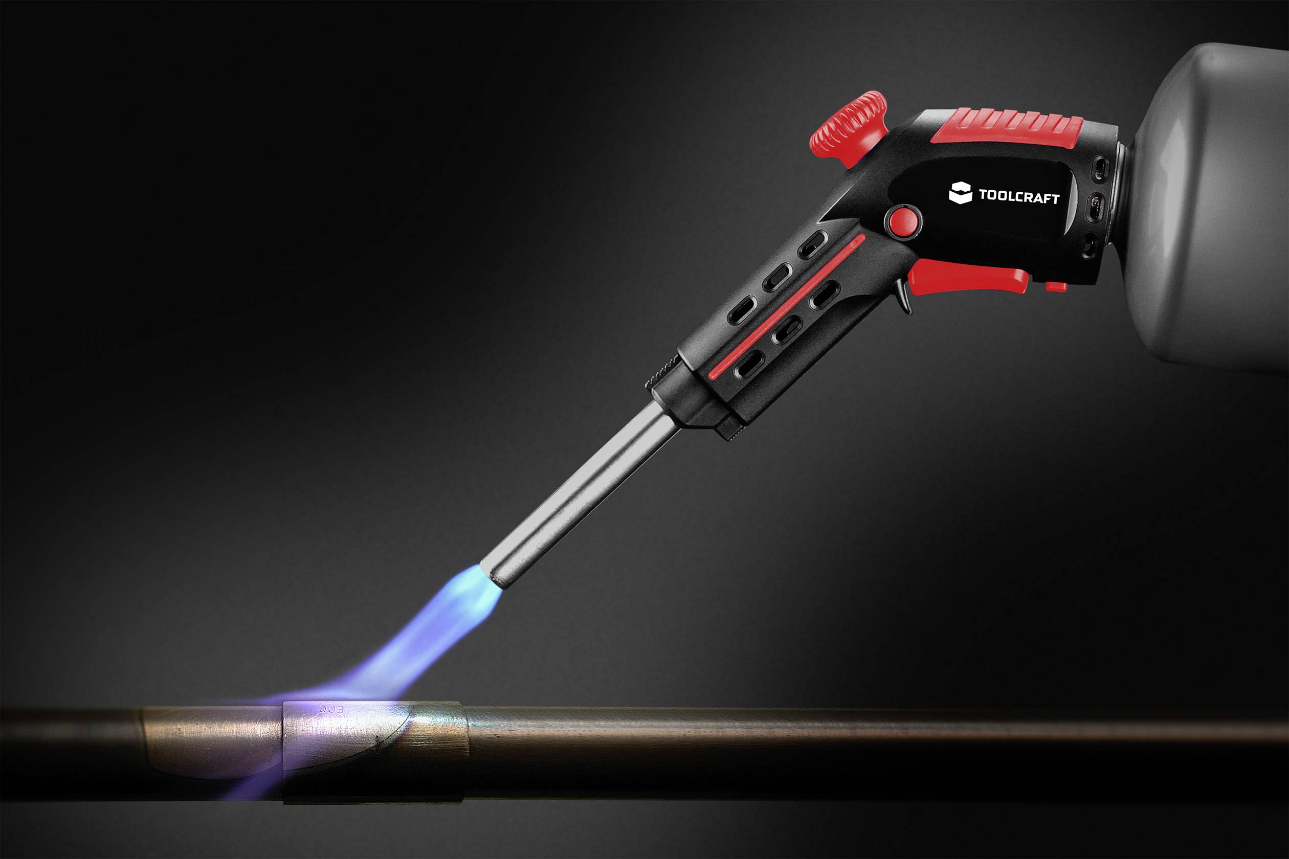 Soudeur de Toolcraft chauffant un tube métallique avec un jet de flamme bleue, sur un fond sombre.