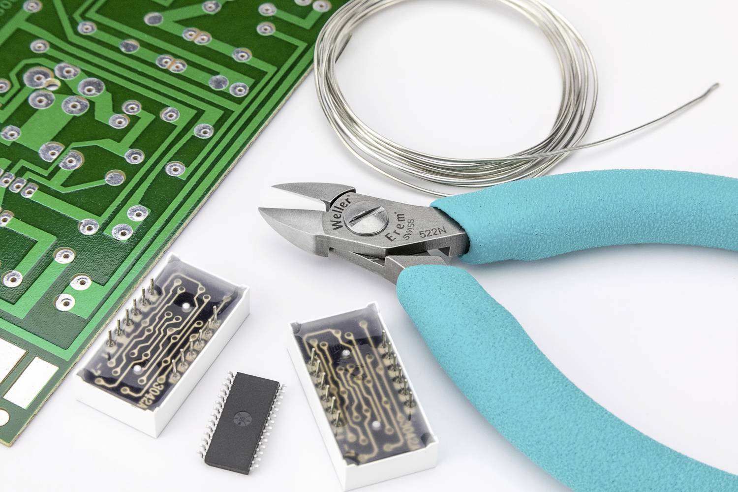 Une carte de circuit imprimé à côté d'une puce, d'un fil et de pinces coupantes bleues, montrant les outils et composants du montage électronique.