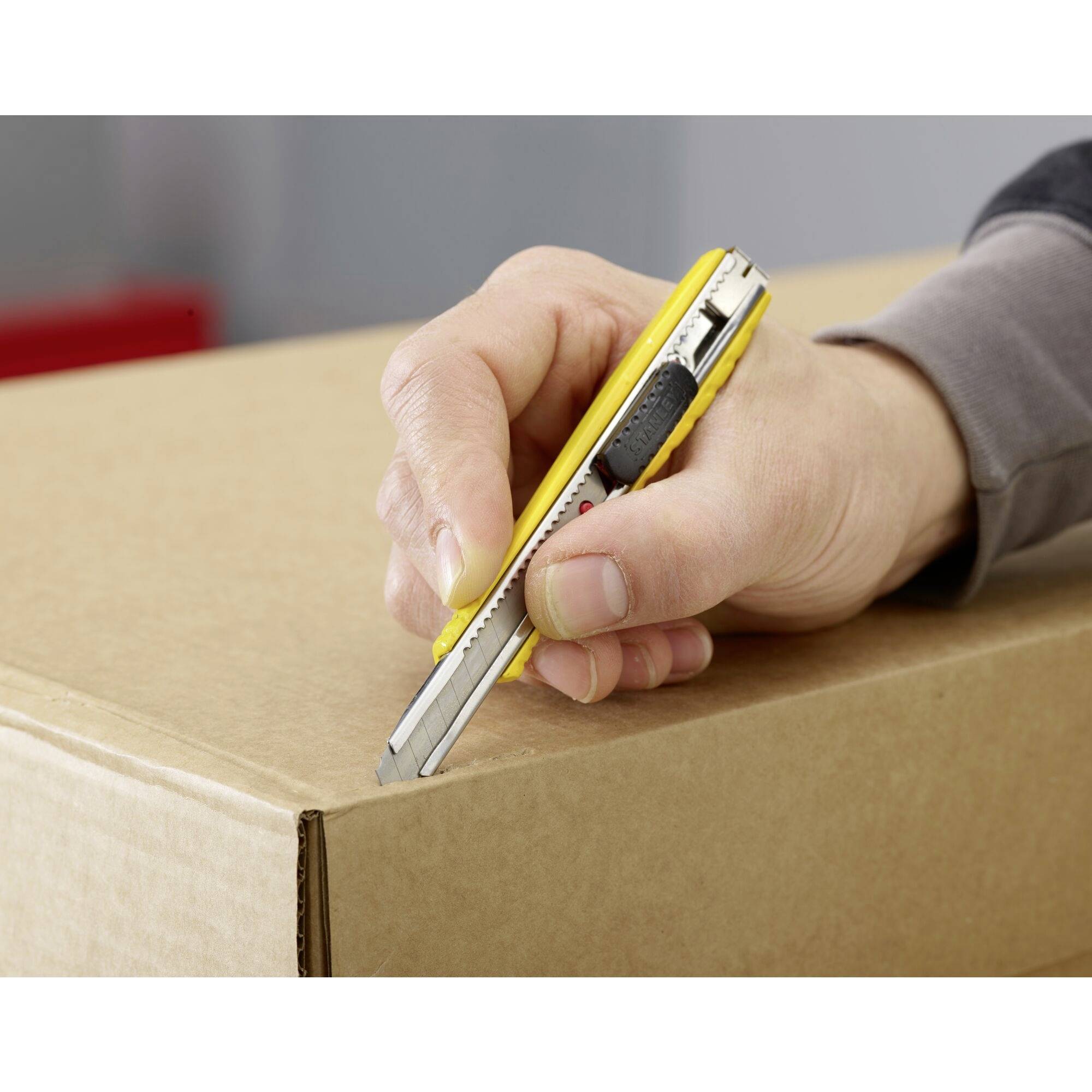 Une main coupe un carton avec un cutter jaune.