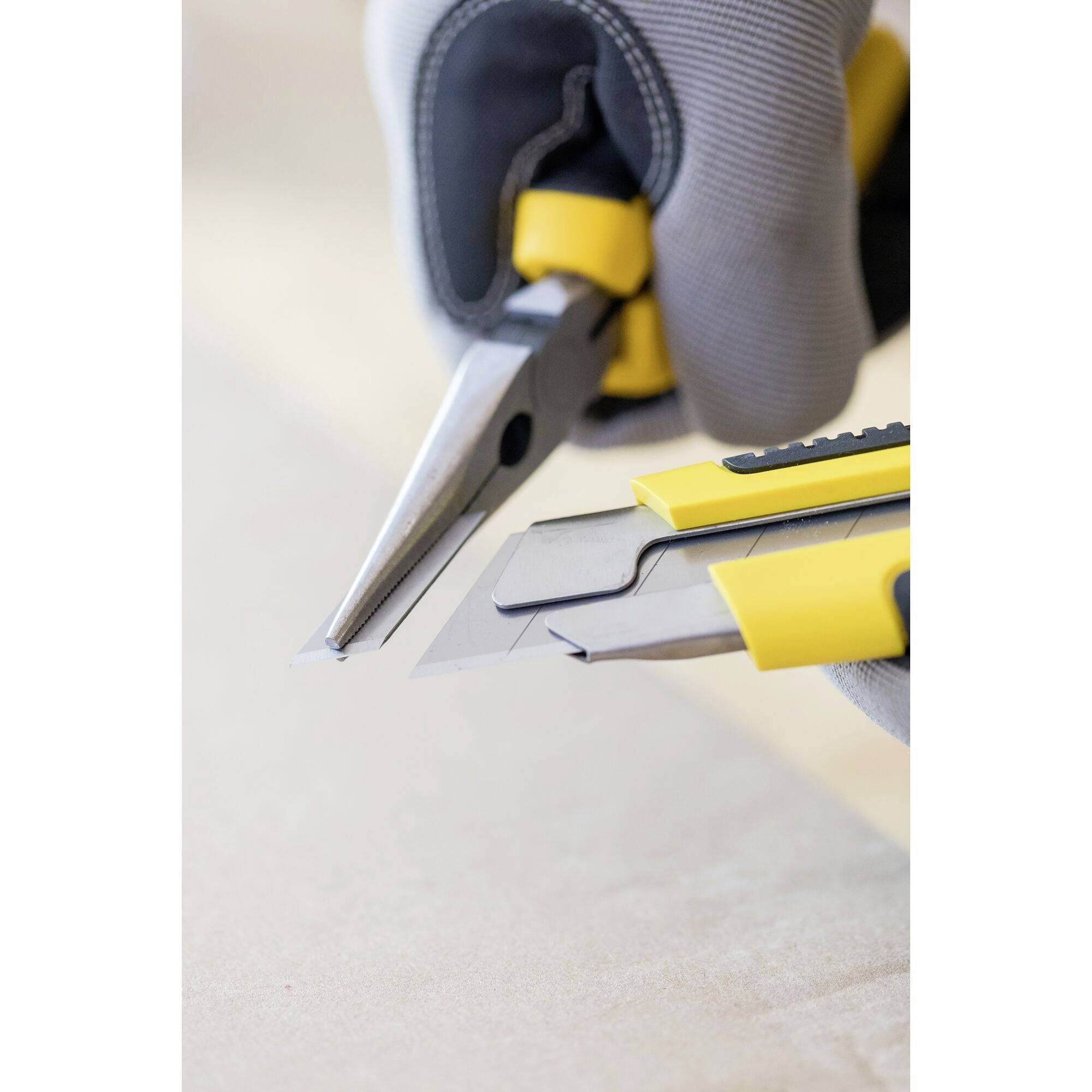 Quelqu'un tient une pince et un cutter, tous deux munis de poignées jaunes. La pince coupe une pièce métallique, symbole de travail manuel.