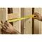 Quelqu'un mesure la distance entre deux poutres en bois à l'aide d'un mètre ruban jaune dans un bâtiment en construction.