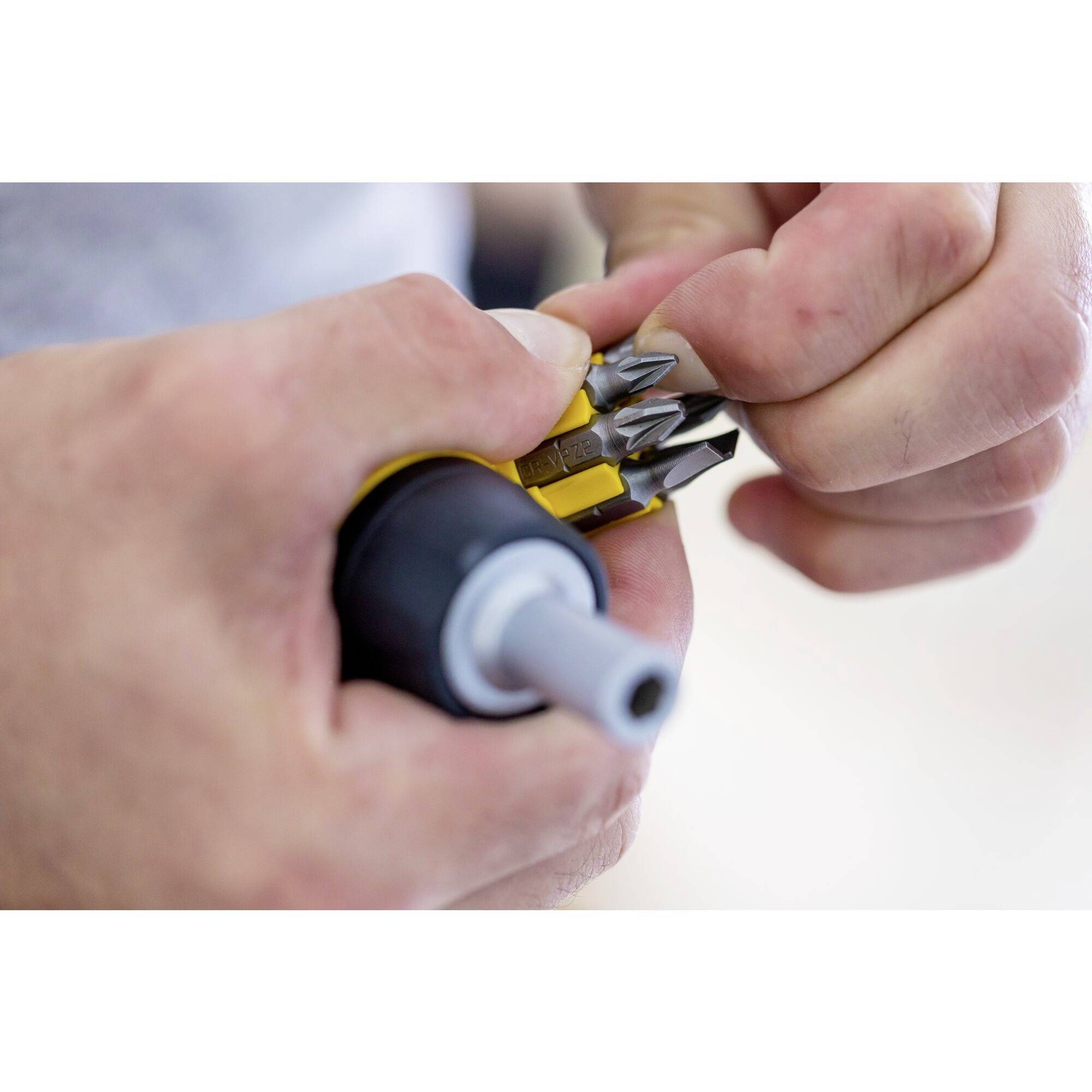 Des mains tiennent un tournevis multifonction avec plusieurs embouts interchangeables. Une personne est en train de changer un embout.